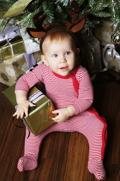 Babymeisje met de geschenkdoos in de buurt van kerstboom versieren. Vrolijke tijd.