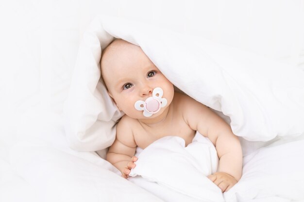 Babymeisje met een fopspeen in een deken in een wieg op een wit katoenen bed zes maanden oud
