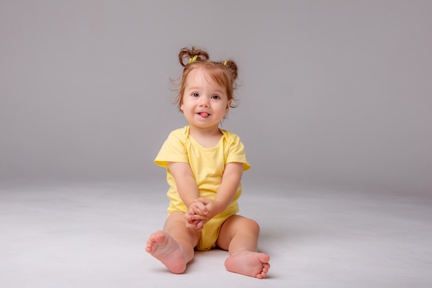 Babymeisje met gele bodysuit zittend op een witte achtergrond