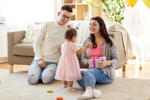 babymeisje met verjaardagscadeau en ouders thuis