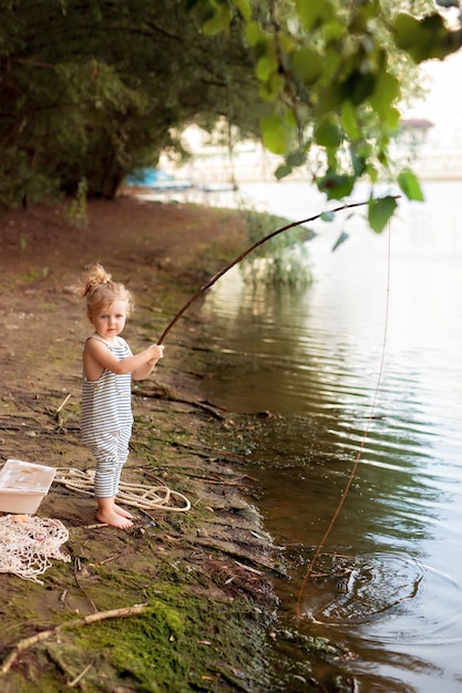 Babymeisje op een zandstrand in de buurt van de rivier houdt een hengel vissen