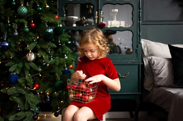 Babymeisje speelt met kerstversiering in de buurt van de kerstboom binnenshuis Prettige kerstdagen en fijne feestdagen