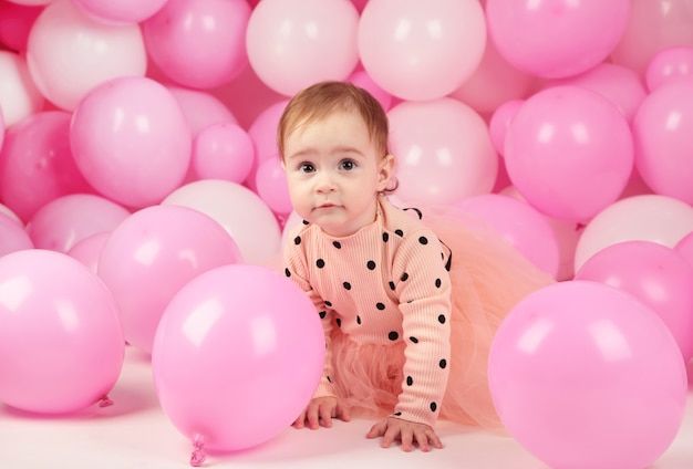 Babymeisje viert haar eerste verjaardag. Meisje op achtergrond van roze ballonnen. Bovenaanzicht