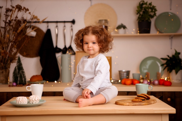 Babymeisje zit in de keuken van kerstmis op tafel