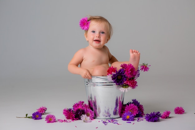 babymeisje zit in een emmer bloemen