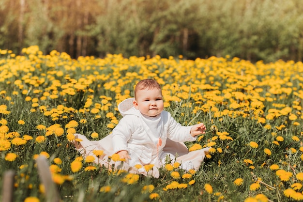 Babymeisje zit op een veld met paardebloemen op een zonnige dag