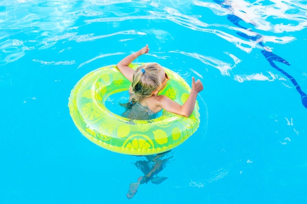 Babymeisje zwemt in het zwembad met een opblaasbare gele cirkel in de zomer en toont klasse, achteraanzicht, reis- en vrijetijdsconcept