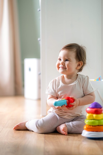 Babyspel klein slim Kaukasisch kind dat kleurrijke plastic speelgoedpiramide speelt die op de vloer zit thuis games voor vroege ontwikkeling kinderen vrije tijd