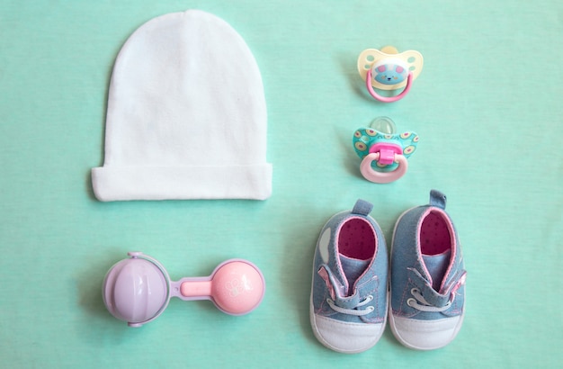 Babyspullen staan op een blauwe achtergrond. bovenaanzicht close-up. dingen klein meisje, fopspeen, rammelaar, hoed en schoenen. pasgeboren baby benodigdheden