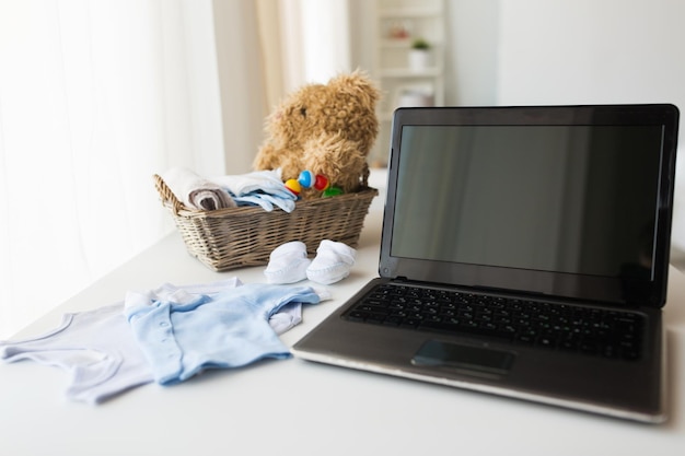 babytijd, moederschap, kleding, technologie en objectconcept - close-up van babykleding en speelgoed voor pasgeboren jongen in mand met laptop thuis