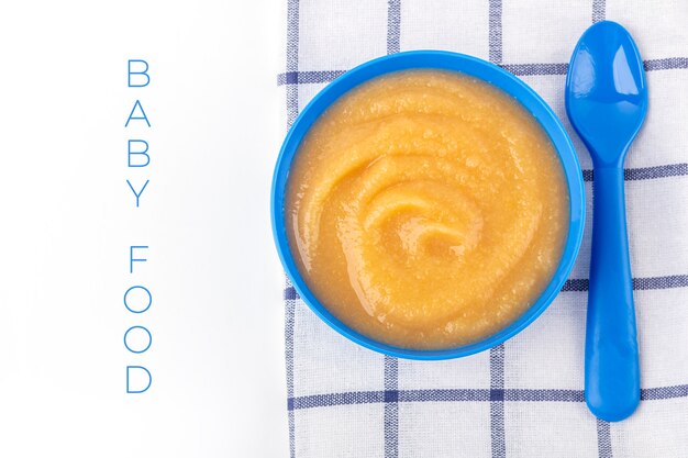 Babyvoedsel. Verse zelfgemaakte appelmoes. Blauwe kom met fruitpuree op stof en kinderspeelgoed op tafel. Het concept van goede voeding en gezond eten. Biologisch en vegetarisch eten. Ruimte voor tekst kopiëren