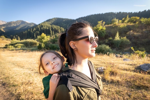 Babywearing woman with her daughter in ergonomic baby carrier travel in mountain