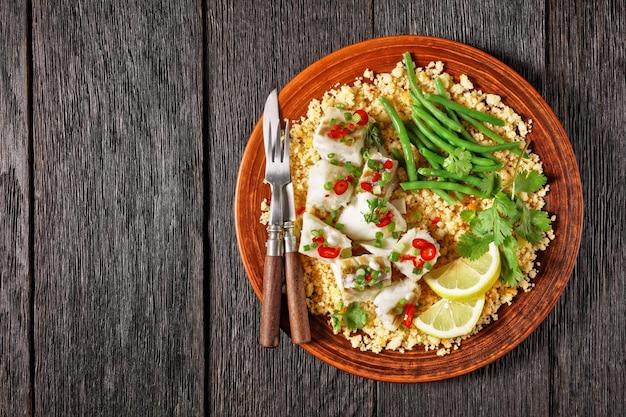 Bacalhau com todos cod with bulgur steamed green beans sprinkled with hot chili peppers and spring onions on a rustic plate on a wooden table portuguese cuisine flat lay free space