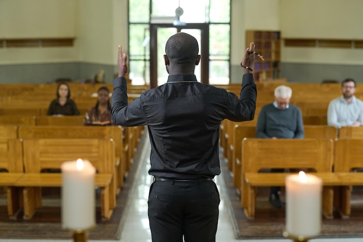 Photo back of african american priest in black shirt and pants blessing parishioners
