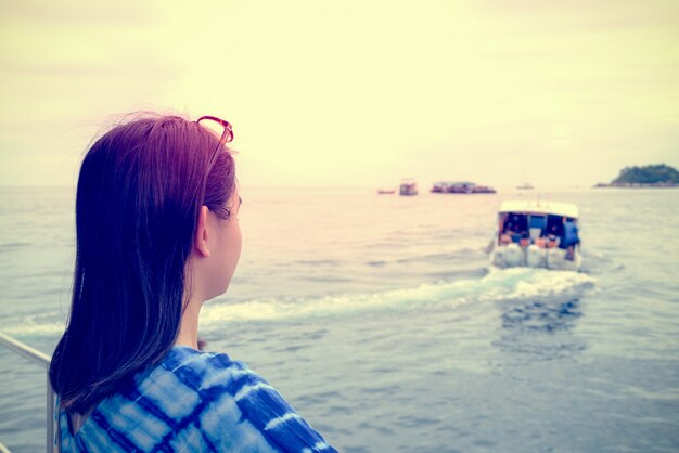 Photo back of asian woman looking at the speed boat that sailed away from her, with a lonely, solitary, sad atmosphere during sunset in vintage style