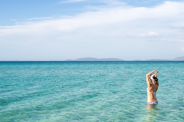 Foto indietro di bella donna che indossa bikini blu in piedi in acqua sulla costa del mar mediterraneo, cesme, spiaggia di ilica, turchia.