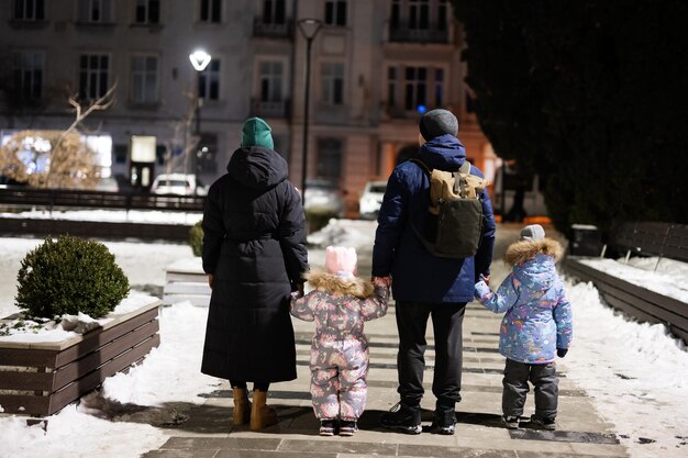 Задняя часть семьи с двумя детьми гуляет по ночному городу зимой