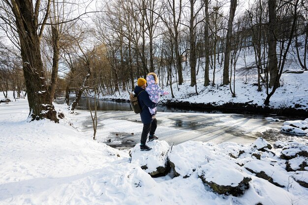 Спина отца и ребенка в солнечный морозный зимний день в парке у реки со скалами