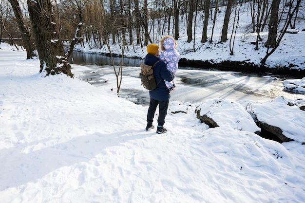 Back of father and child on a sunny frosty winter day in the park near river with rocks