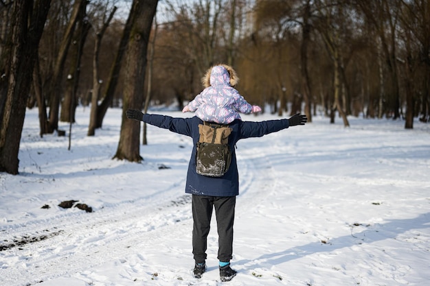 Back of father hold child on shoulders at sunny frosty winter day in the park Dad and daughter love