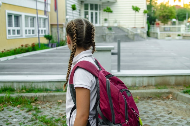 Foto indietro del bambino della ragazza che va a scuola con zaino rosso.