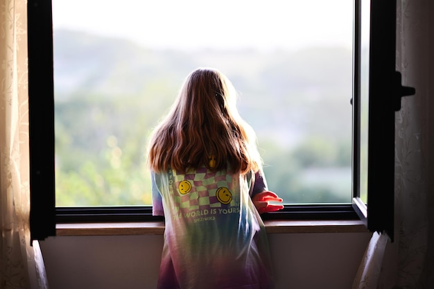 Photo back of girl looking from window in sunset