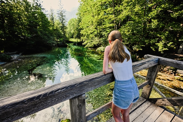 줄리안 알프스 Ukanc 슬로베니아의 에메랄드 녹색 물 강 Sava Bohinjka의 나무 다리에 소녀의 뒤
