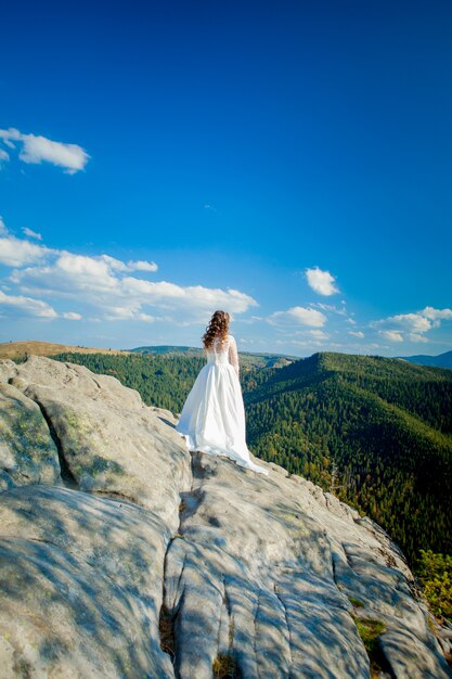 Photo back of girl in wedding dress sitting on rocks in mountains and looking to fjord, hiking in hills