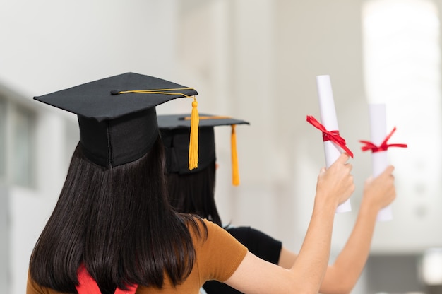 The back image of a female college student graduates wearing a black hat yellow tassel