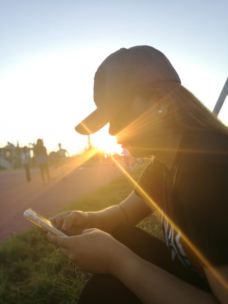 写真 空に向かって携帯電話を使っている背中を照らした女性