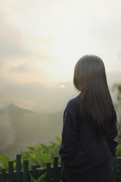 스웨터를 입은 긴 머리의 소녀의 뒷면은 주변 산의 전망을 바라보고 있습니다.