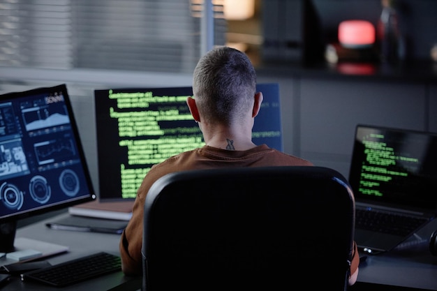 オフィスで遅くまで働くコンピューターで机に座っている男性のIT開発者の背中