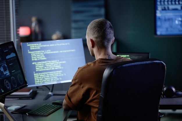 オフィスのワークステーションでコンピュータを使用する男性ソフトウェア開発者の背面