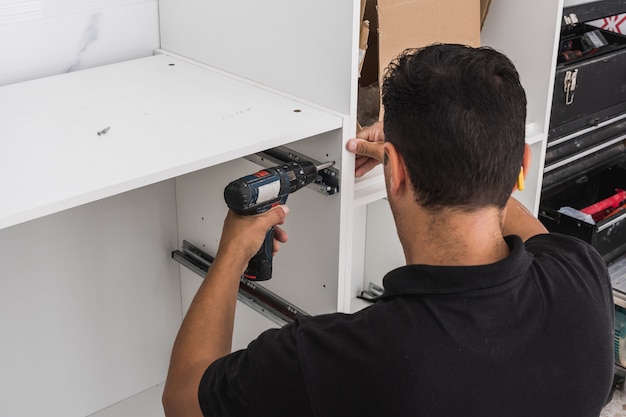 Back of a man assembling a kitchen with a drill