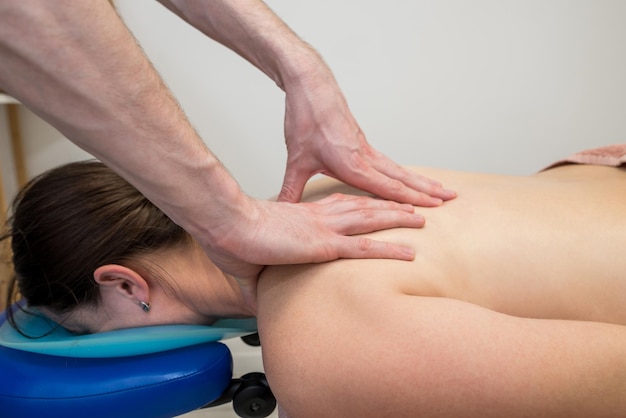 Back massage in a massage parlor Body care concept A professional massage therapist massages the back of a young woman lying on a massage table