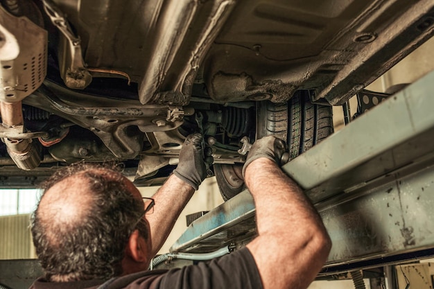 Back of a mechanic under a car lifted by a jack fixing steering alignment in a workshop