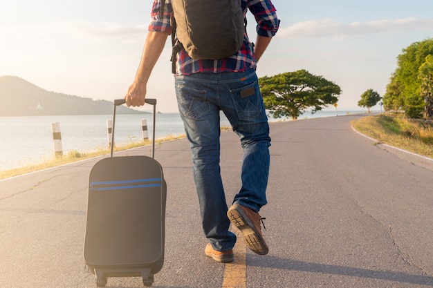 Foto la parte posteriore dei turisti uomini a piedi trascinando i bagagli sulla strada. il concetto di viaggio.