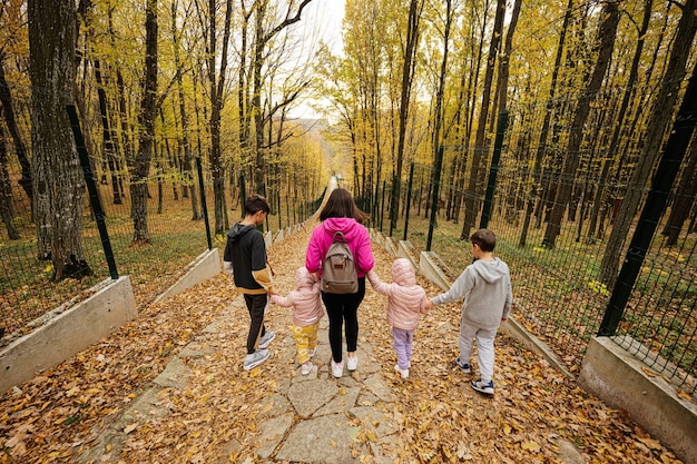 Back of mother with four kids on path at autumn fall forest