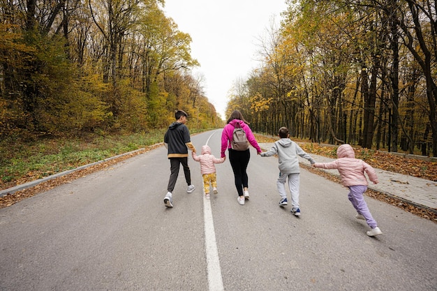 Back of mother with four kids running on road at autumn fall\
forest