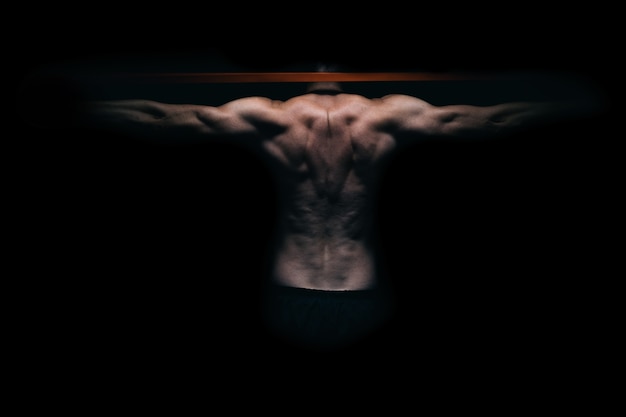 Back of a muscular man exercising with an elastic band