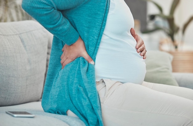 Back pain pregnancy and woman relaxing on a sofa in her living room at her modern house Medical emergency injury and pregnant lady with a swollen body physical inflammation and backache at home