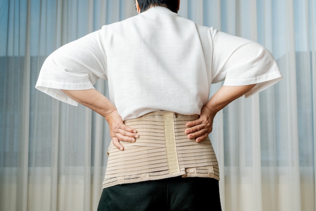 Back pain, senior woman wearing back support belt on white\
background