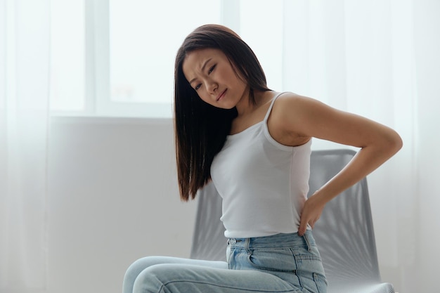 Back pain suffering from osteochondrosis after long study work\
pretty young asian woman touching painful lower back at home\
interior living room injuries poor health illness concept cool\
offer
