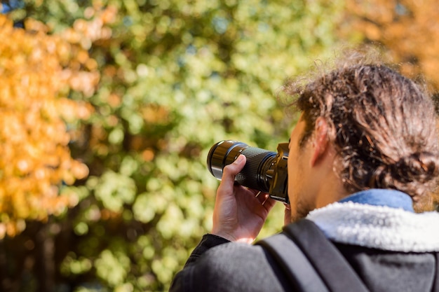 写真 秋の公園を撮影している写真家の後ろの写真。写真に秋の季節を描くコンセプト