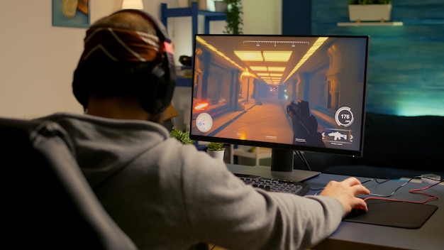 Photo back of pro gamer playing first person shooter video game on professional computer for cyber esport competition. pro player talking with multiple players using headset during online tournament