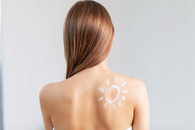 Back behind rear view of young adult woman applying body cream on shoulder