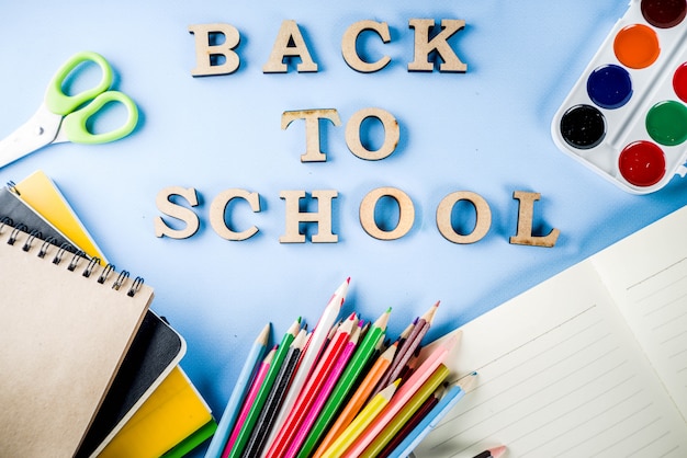 Back to school background with accessories for the schoolroom - paints, pencils, notebooks, books, scissors, chalk, markers, blue background, above copy space