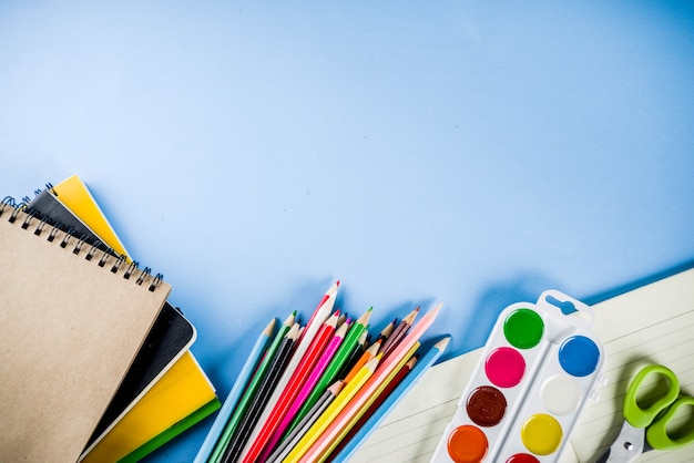 Back to school background with accessories for the schoolroom - paints, pencils, notebooks, books, scissors, chalk, markers, blue background, above copy space