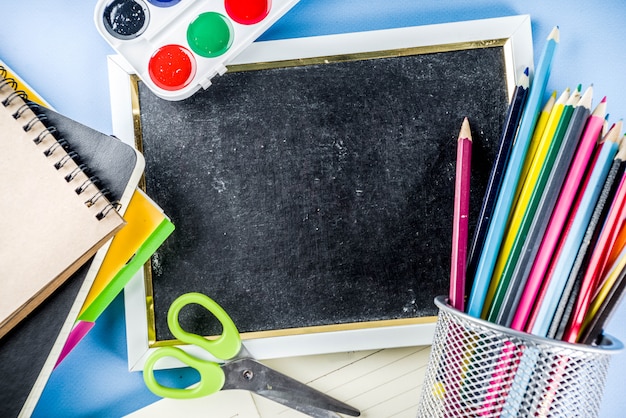 Back to school background with accessories for the schoolroom - paints, pencils, notebooks, books, scissors, chalk, markers, blue background, above copy space