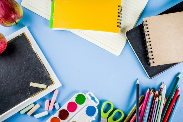 Back to school background with accessories for the schoolroom - paints, pencils, notebooks, books, scissors, chalk, markers, blue background, above copy space